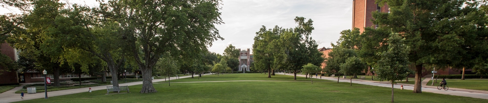The University of Oklahoma’s South Oval &mdash; a broad green lawn framed by mature shade trees and red-brick buildings, with the tower of Bizzell Memorial Library closing the view at the far end.